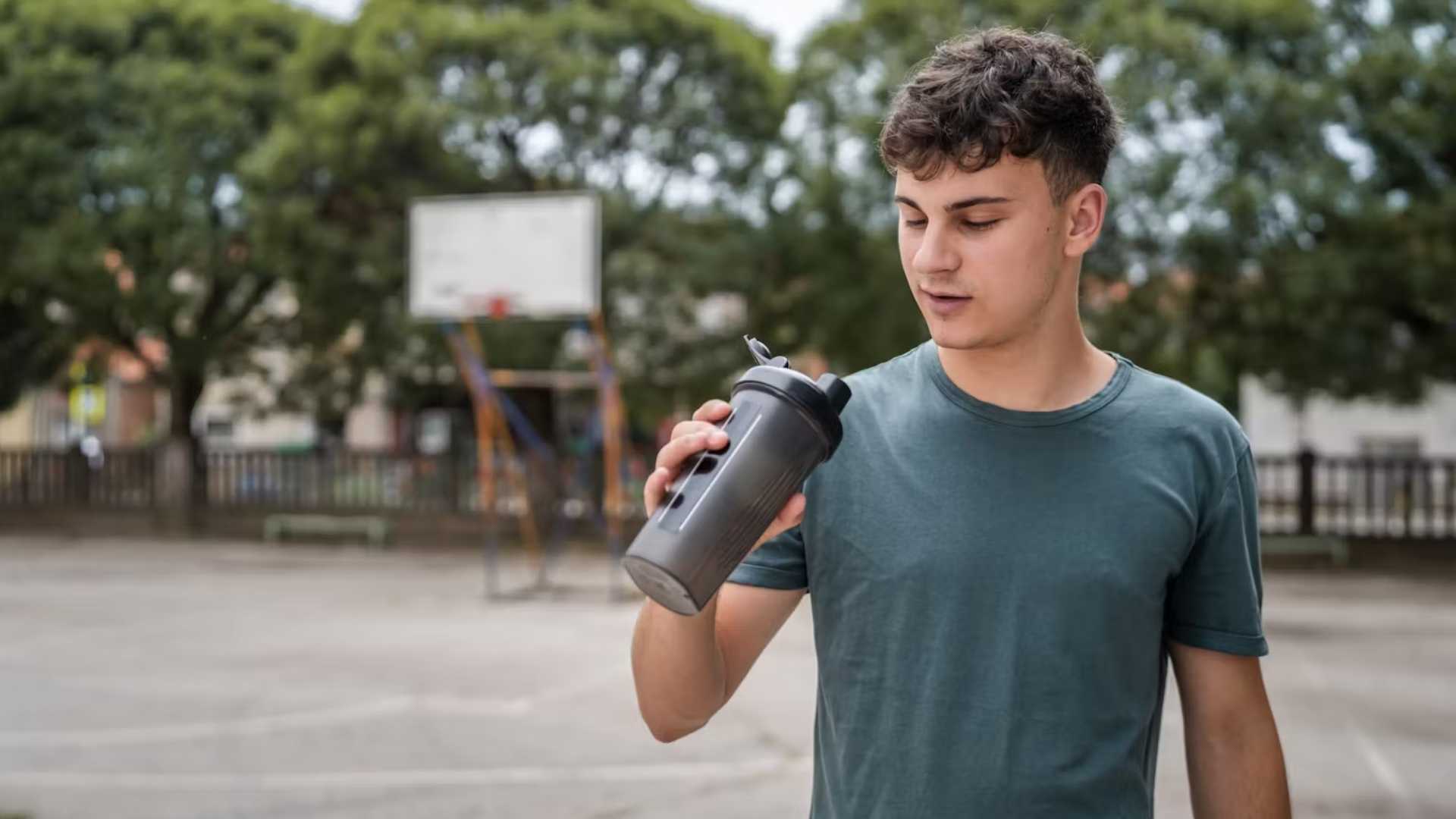 A teenage boy holds a shaker bottle of creatine and water