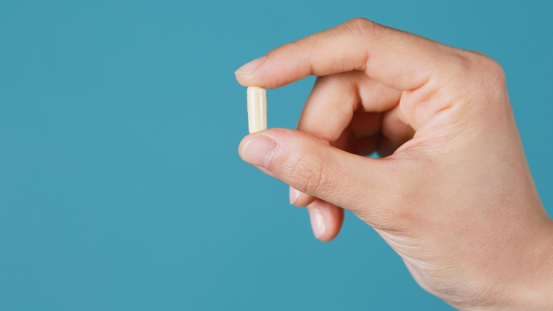 A person holds a pill in between their fingers