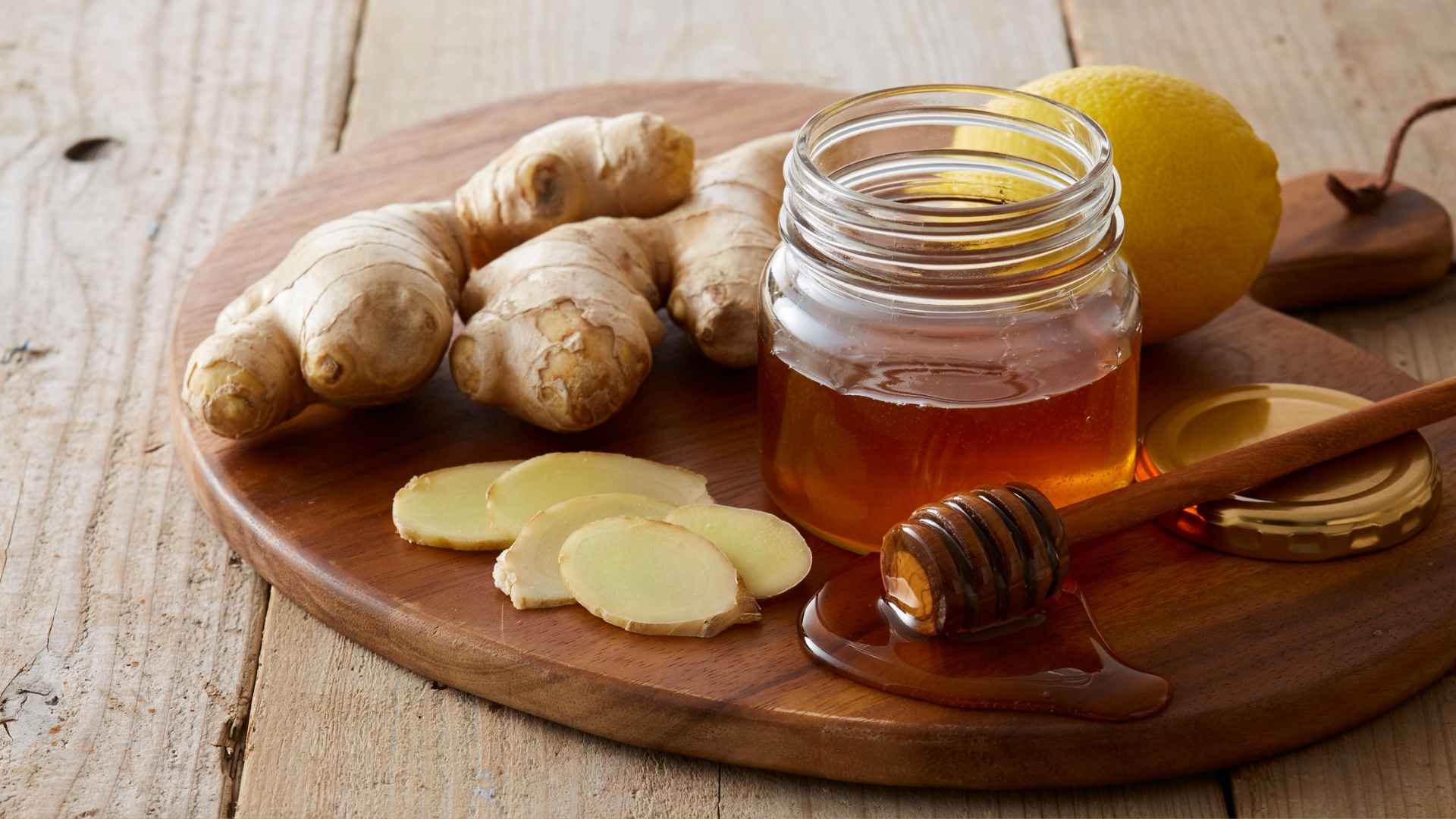 A board with a pot of honey, a lemon, and sliced ginger