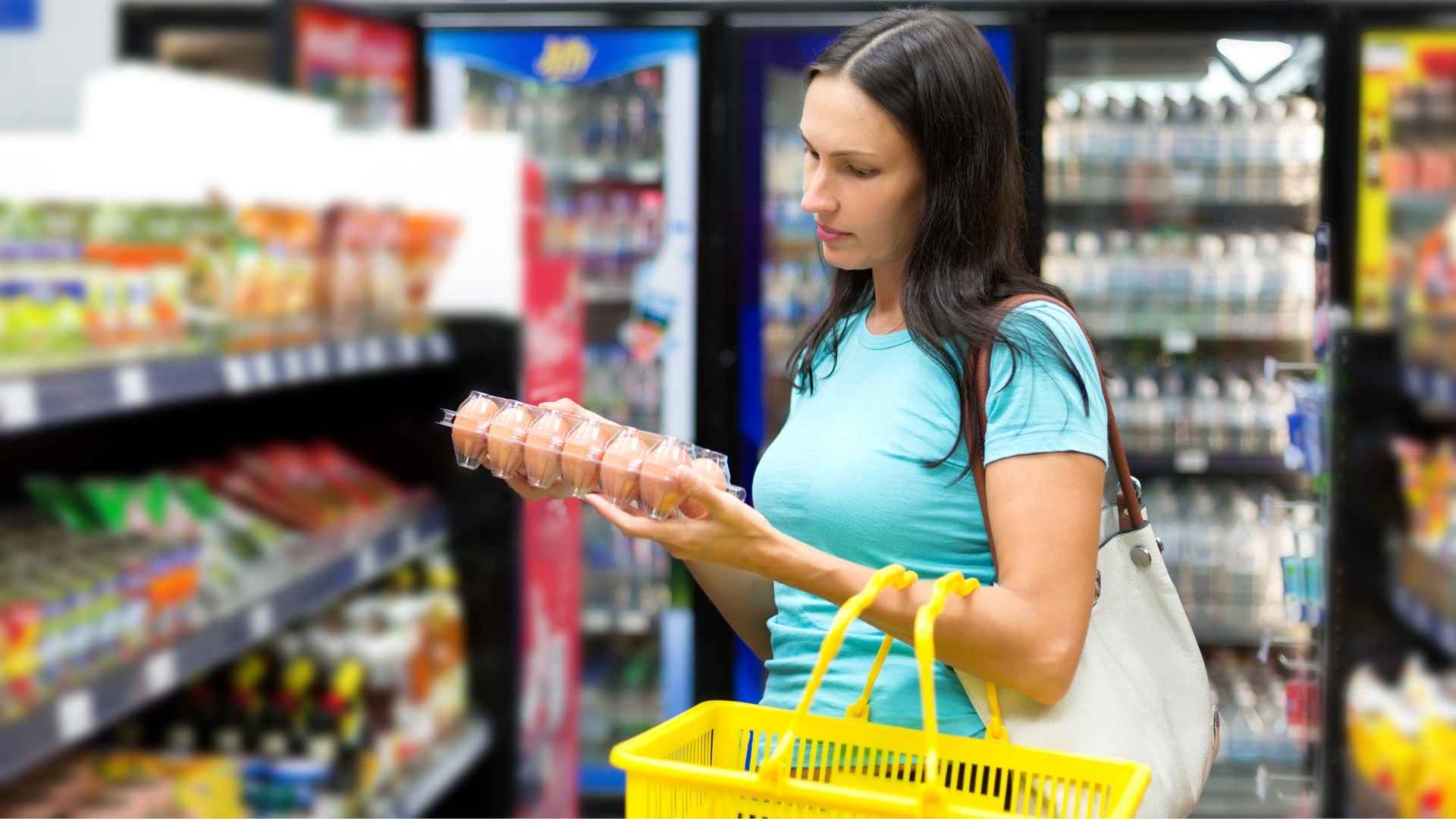 A woman is shopping and holds a carton of eggs
