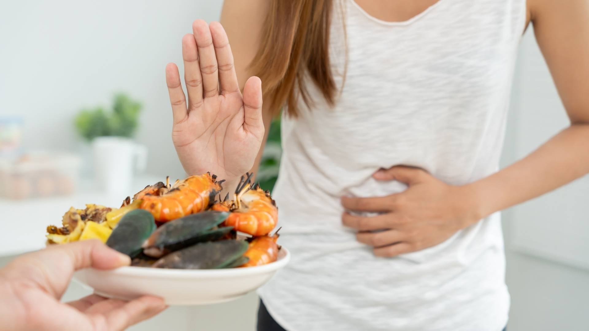 A woman clutches her stomach and holds her hand up to refuse a plate of seafood