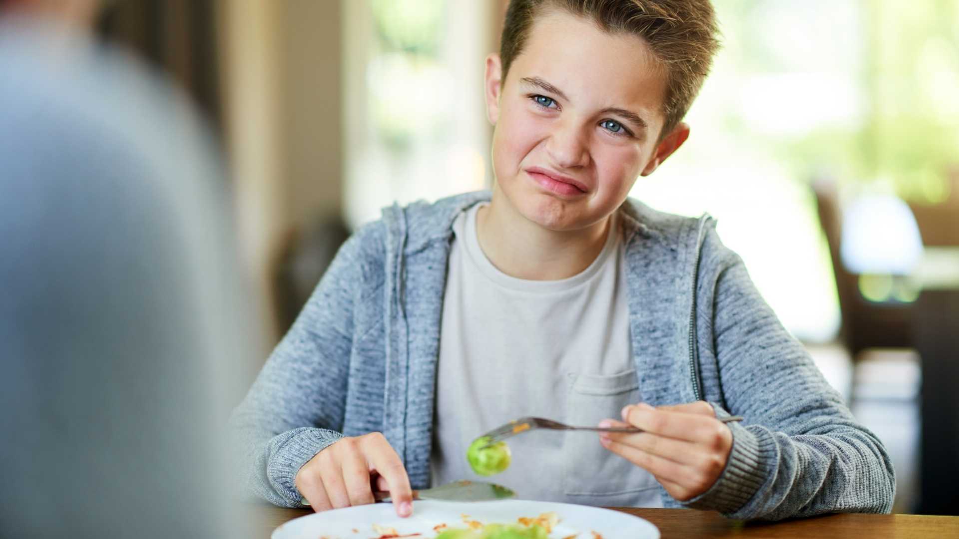 A child holds a Brussels sprouts with a disgusted look on their face