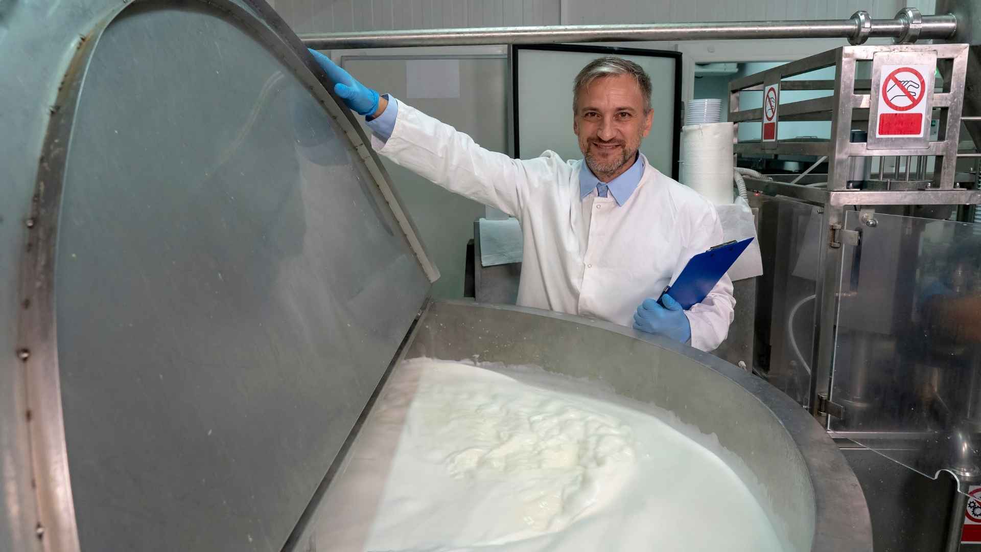 A person in a lab coat stands next to a large vat of milk