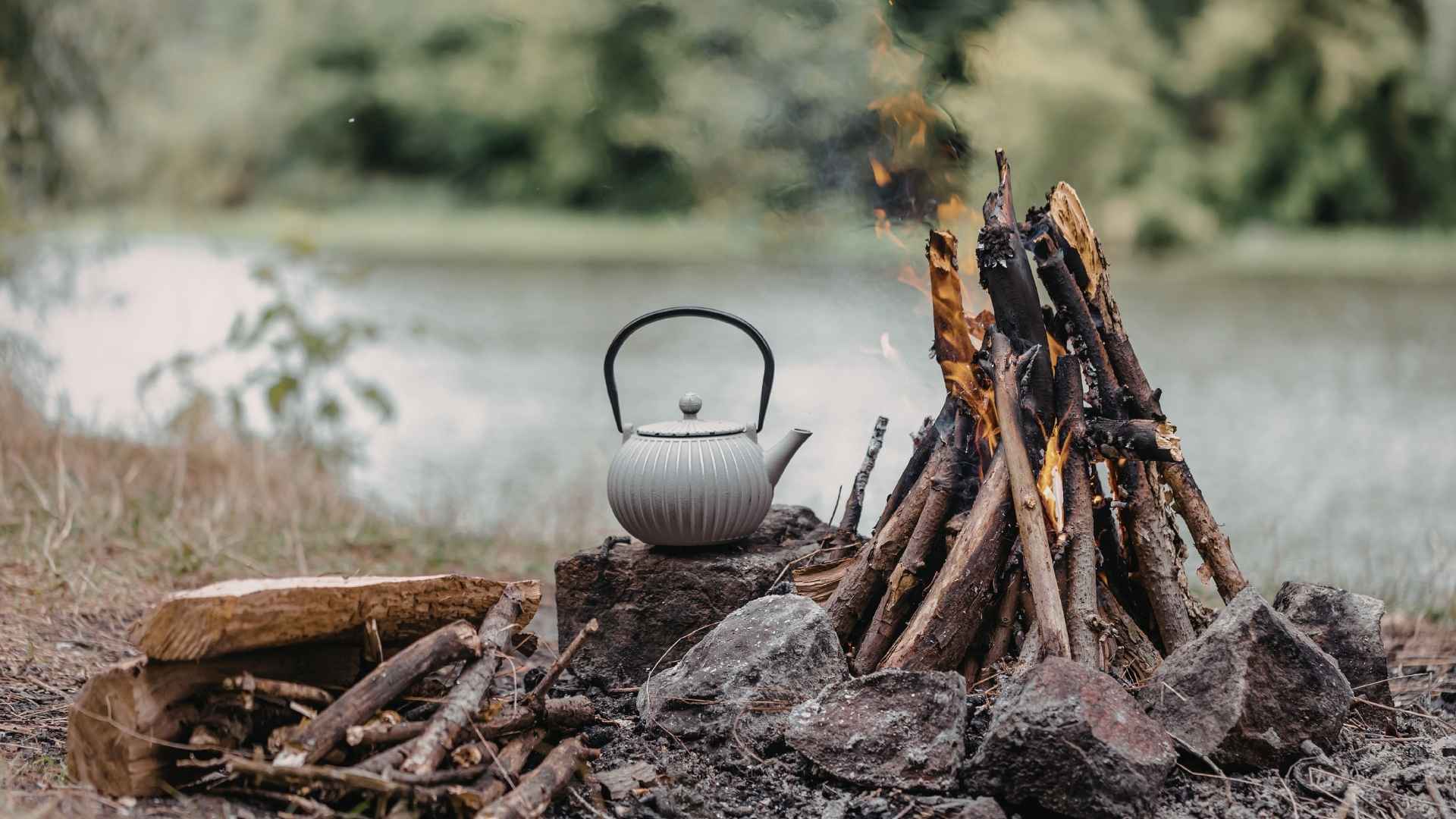 A pot of tea heats up next to a campfire