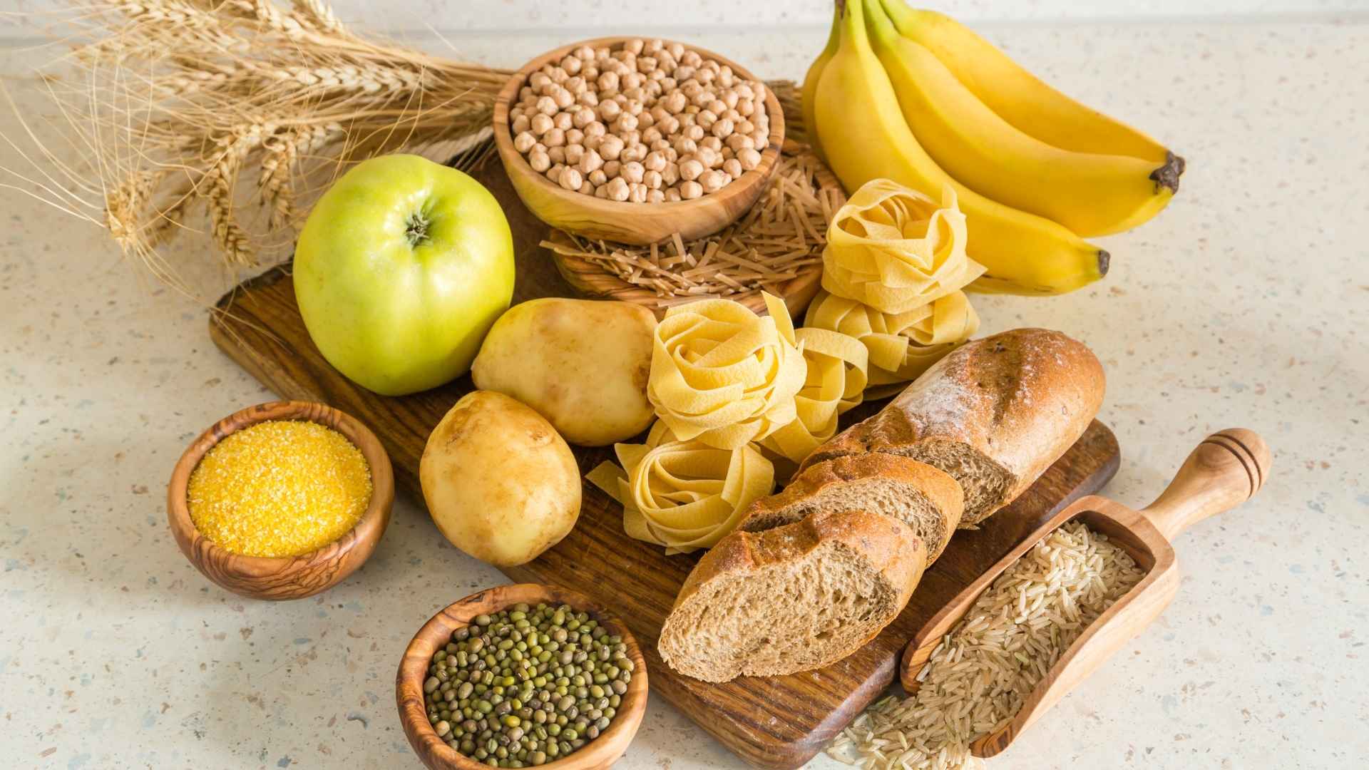 An assortment of carby-foods, such as pasta, bread, legumes, and fruits