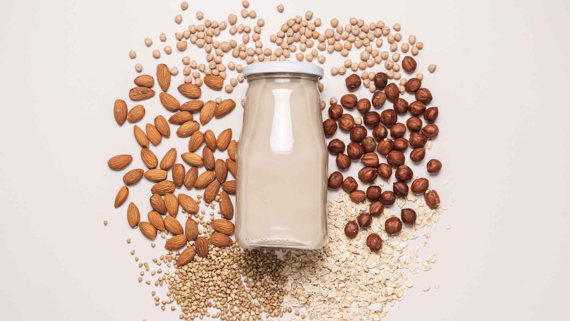 A bottle of milk is surrounding by different nuts and legumes