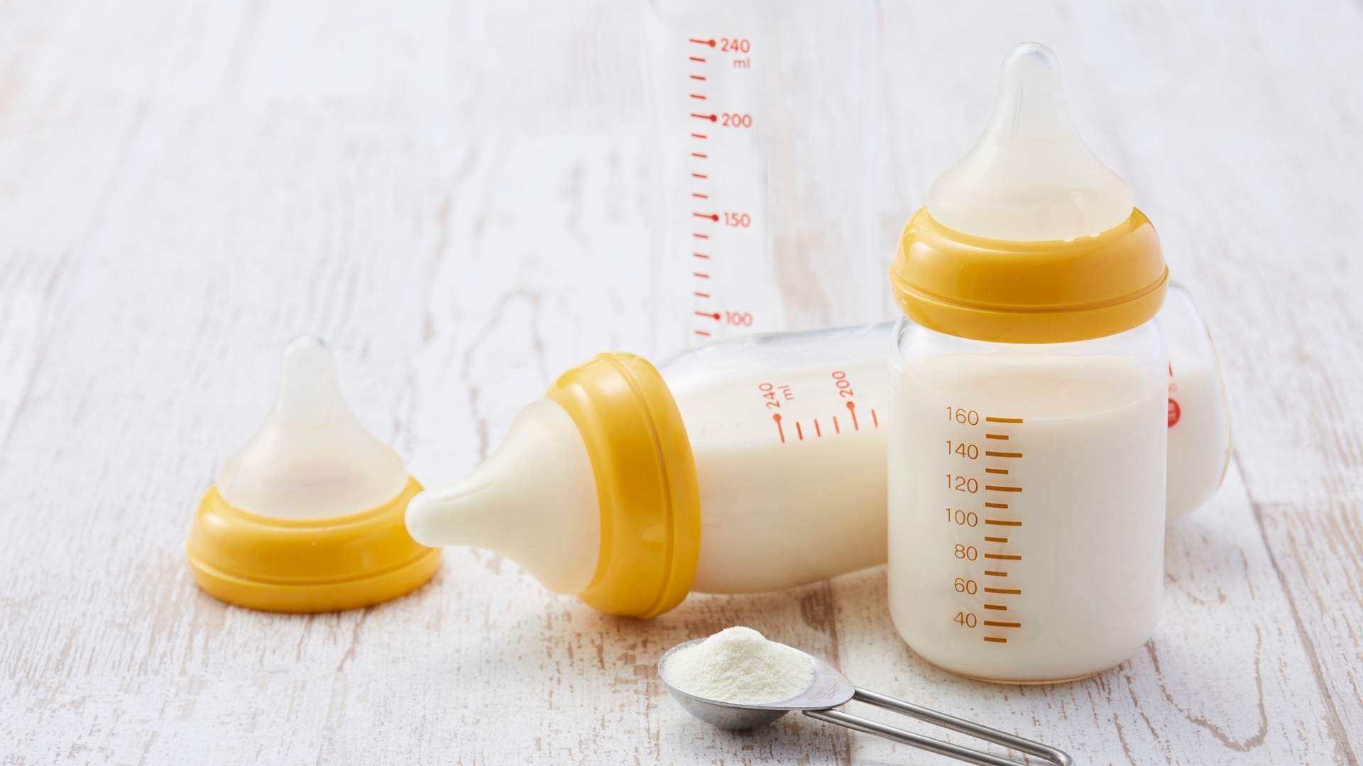Bottles of infant formula are next to a spoon with infant formula powder