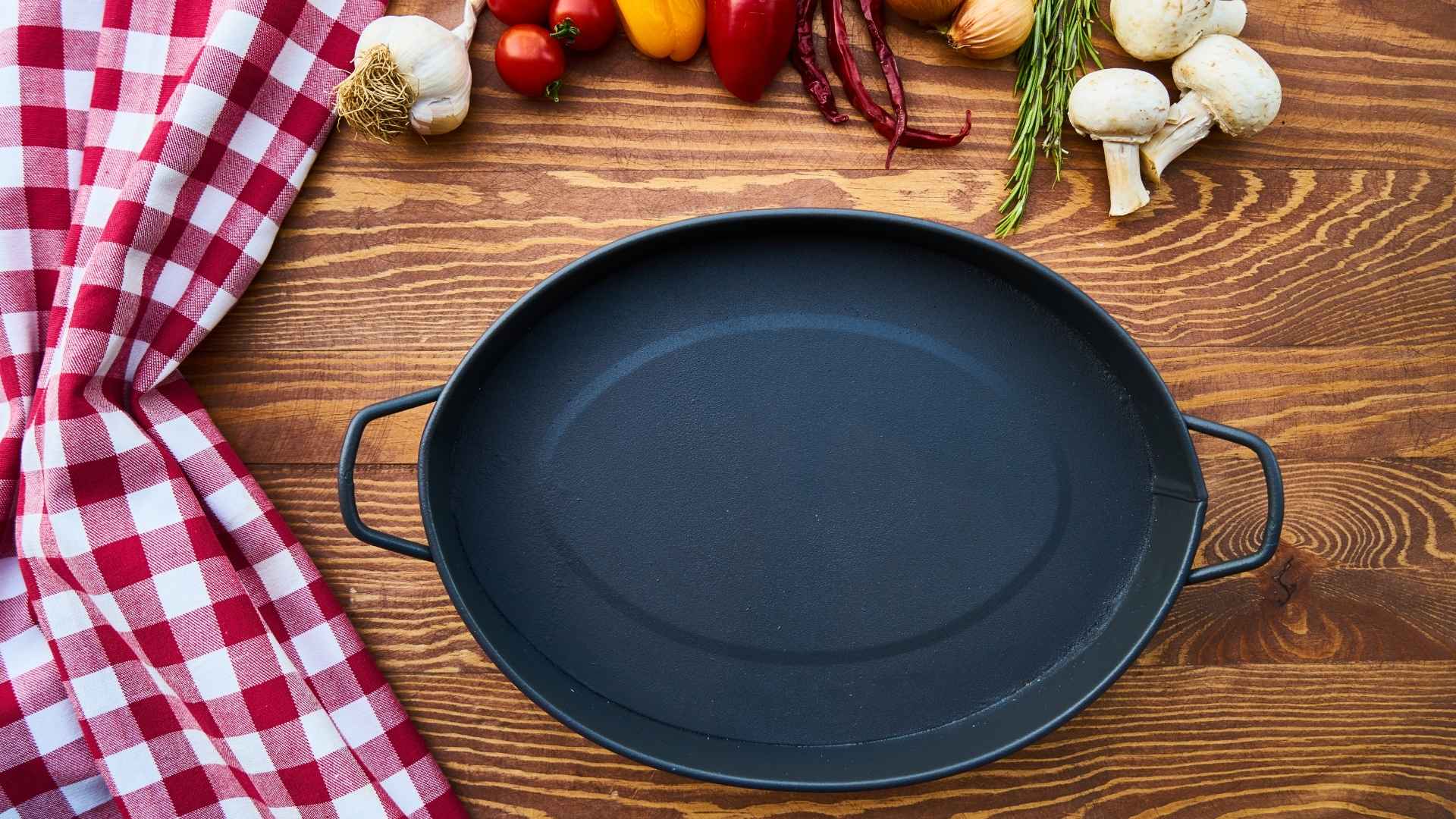 A cast iron skillet is surrounded by vegetables and herbs
