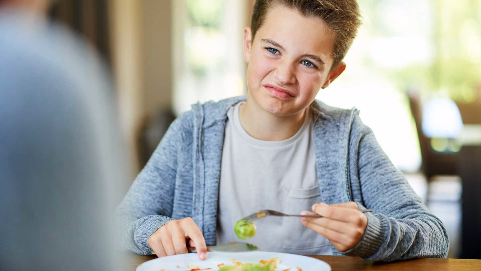 A child holds a Brussels sprouts with a disgusted look on their face