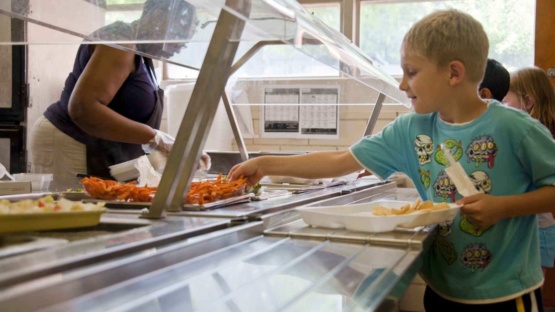A young school child reaches to get some food from the cafeteria