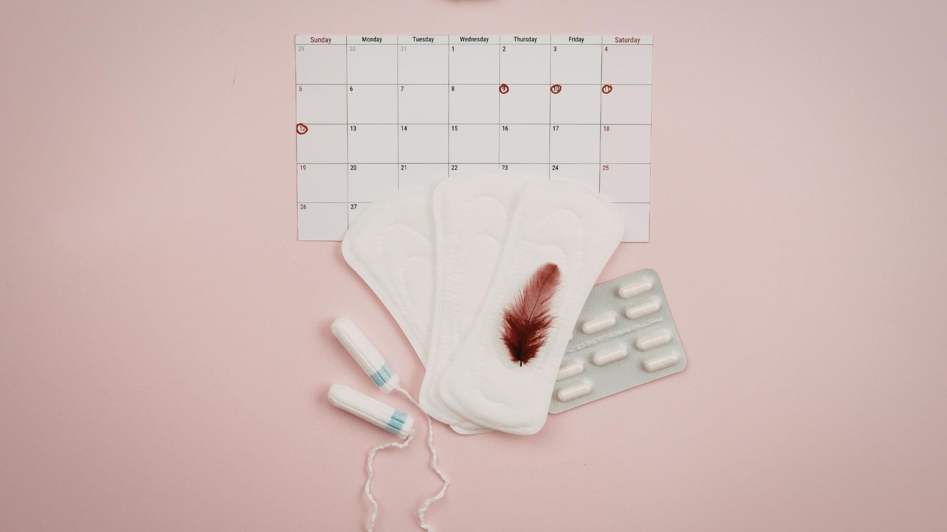 Various menstrual products sit in front of a calendar with certain dates circled