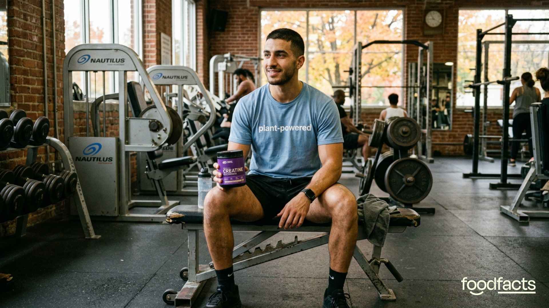 A person wearing a t-shirt reading 'plant-powered' holds a tub of creatine monohydrate