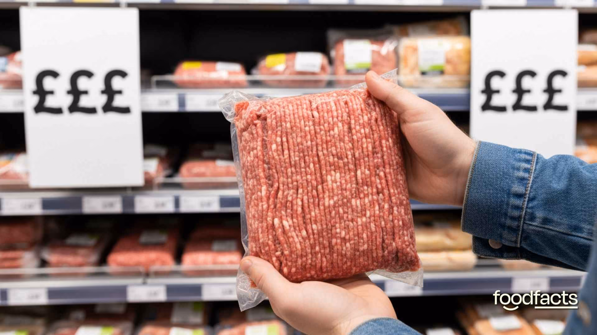 A person holds a packet of minced meat in front of pricing signs that show a very high price