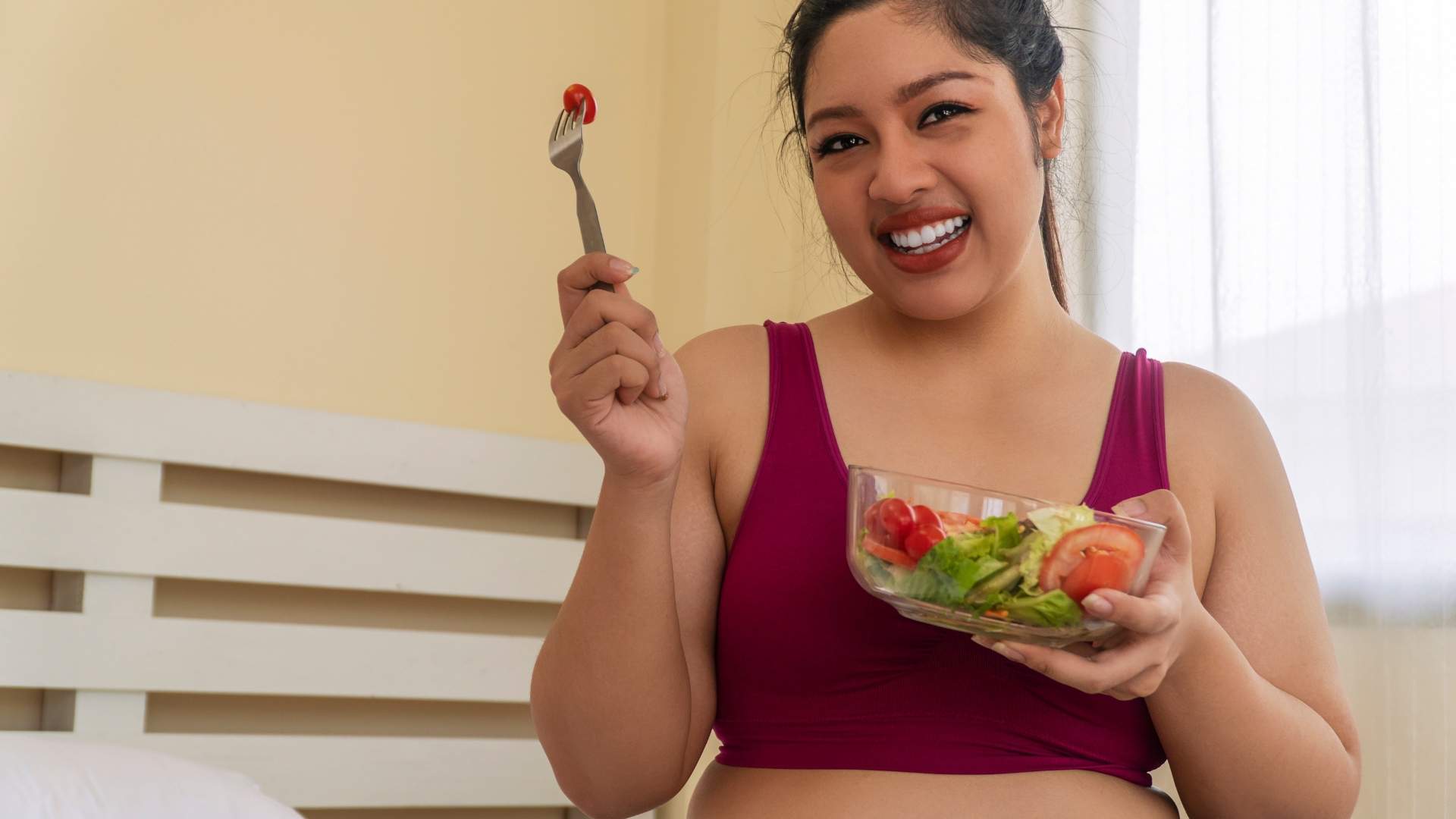 A slightly overweight woman eats a bowl of salad