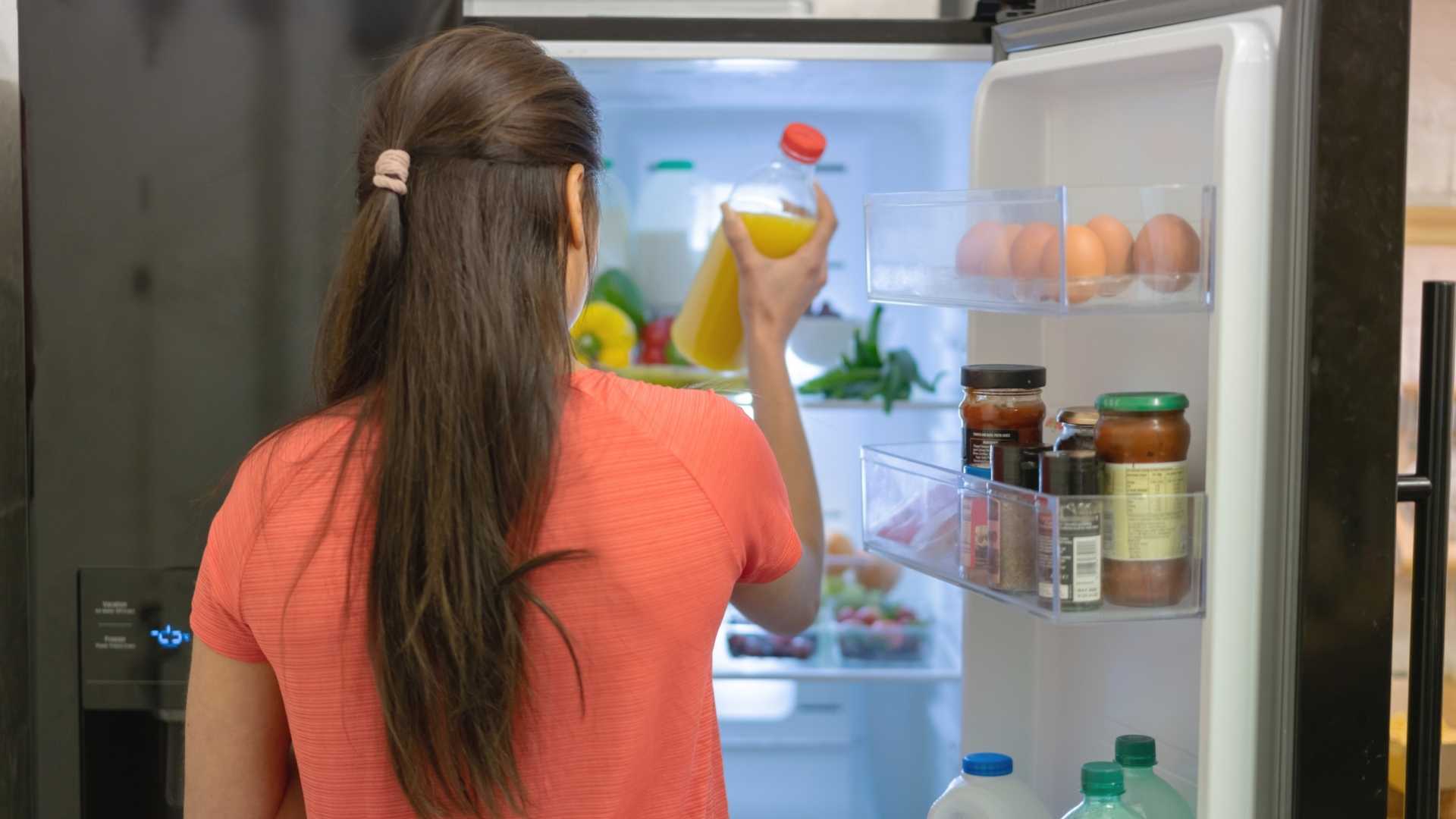 A woman places juice in the fridge