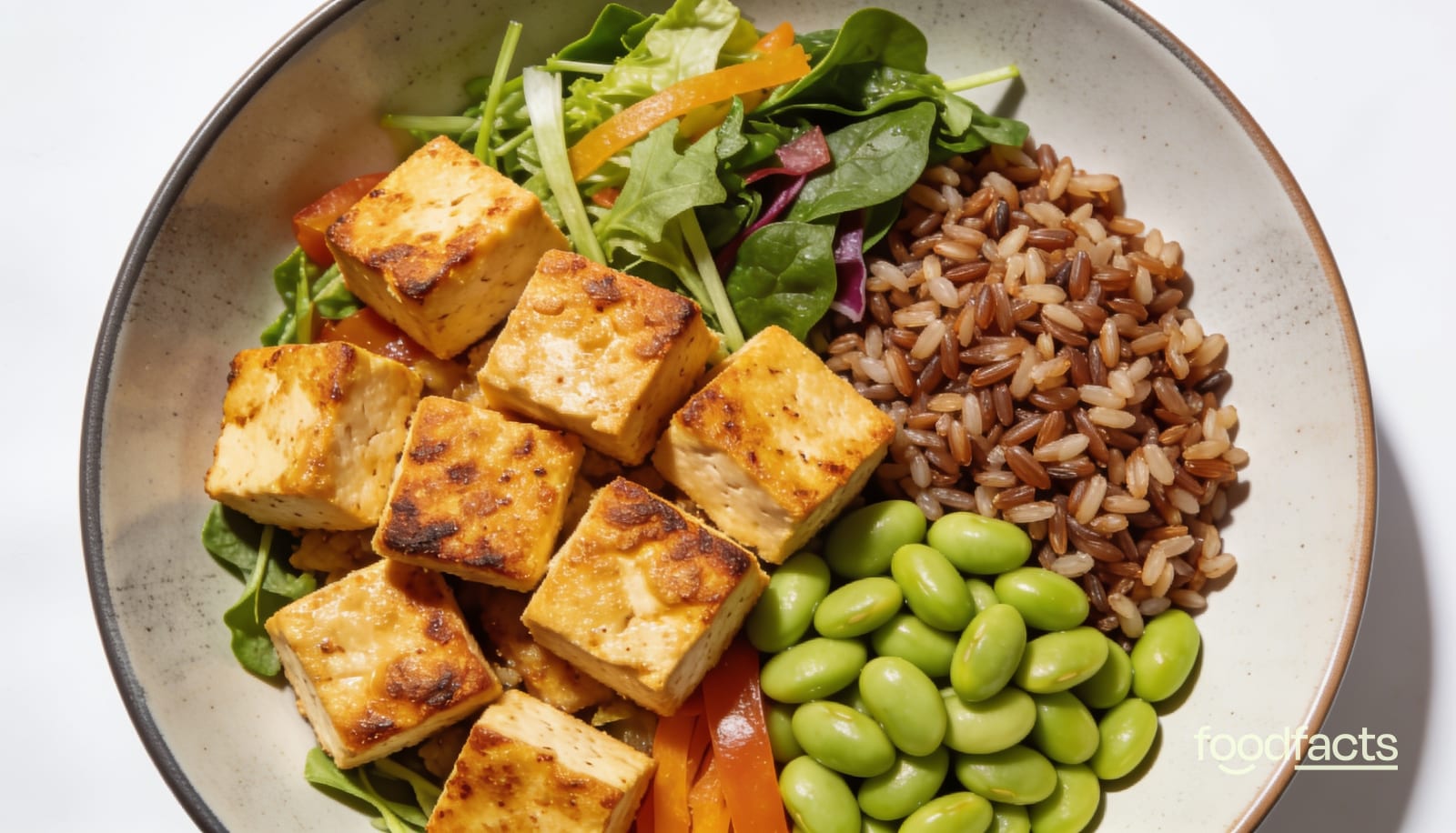A high-protein bowl of golden pan-seared tofu with edamame, brown rice and fresh vegetables