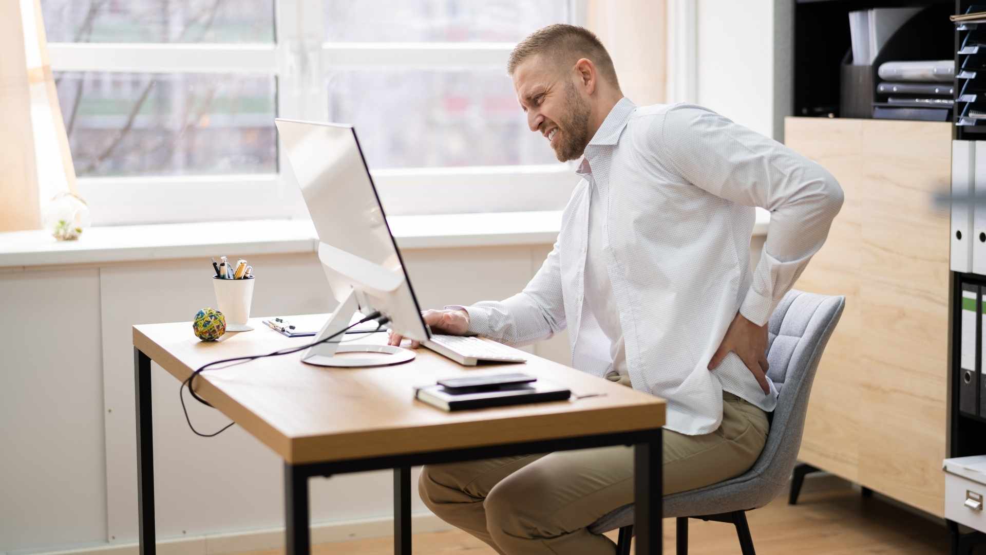 A man sits at a desk with back pain