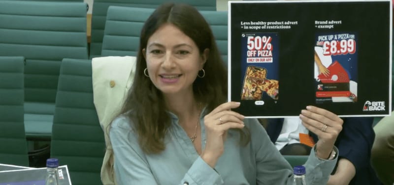 Nika Pajda, Head of Policy and Research at BiteBack 2030, holds up a piece of paper showing pizza adverts