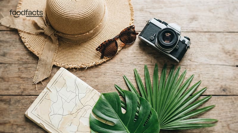 A straw sun hat, sunglasses, a film camera, a folded map and palm leaves on a wooden table
