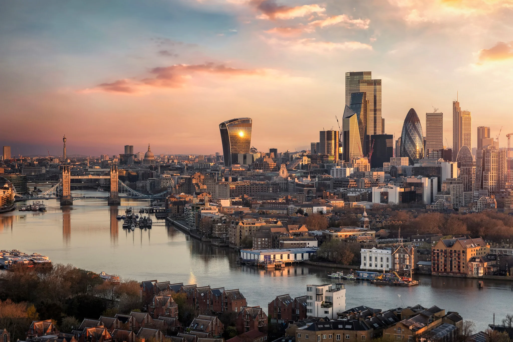 Sunset view of London skyline with the River Thames, Tower Bridge, and iconic skyscrapers including the Walkie Talkie and the Gherkin.