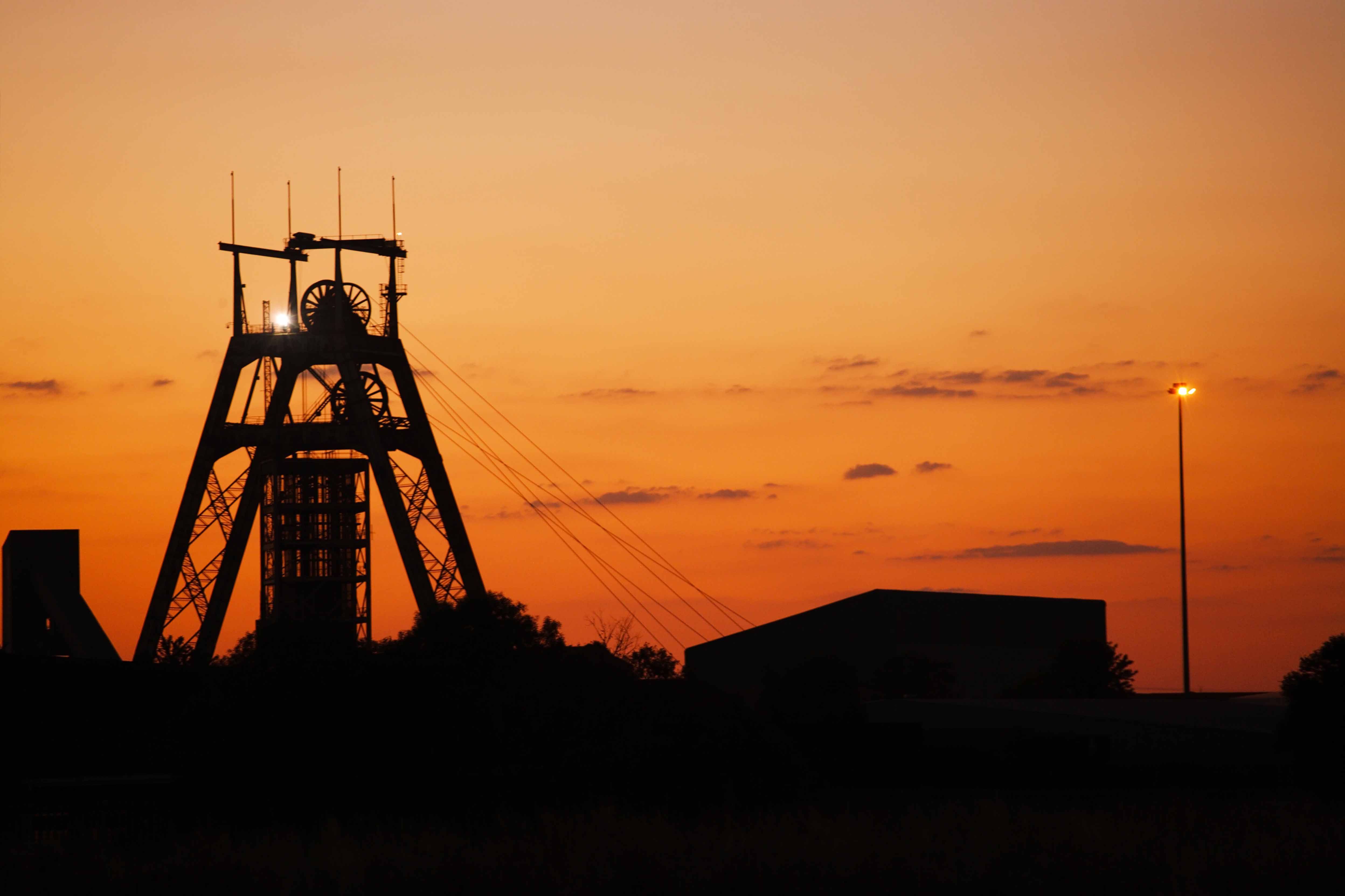 Silhouette of a mine headframe against an orange sunset sky