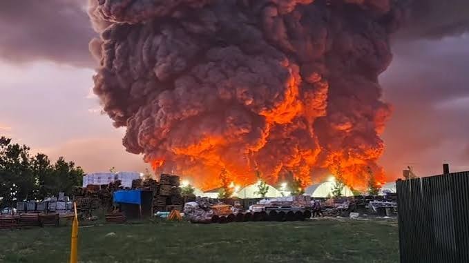 Huge plume of black smoke and flames rising from a burning industrial site at dusk