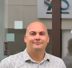 Portrait professionnel d'un homme chauve devant une façade vitrée.