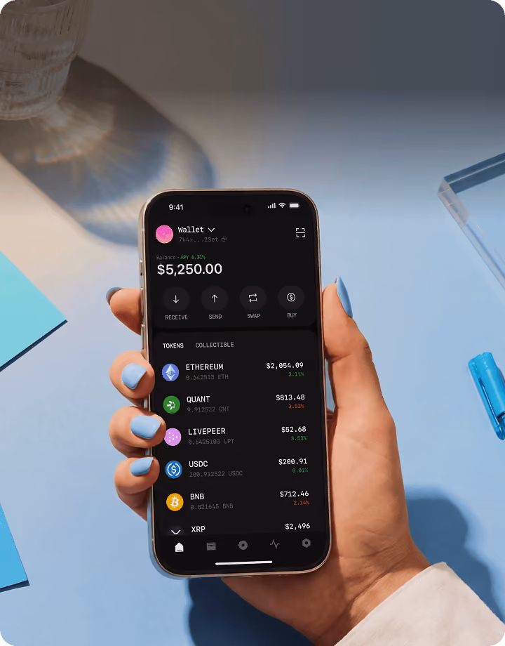 Hand holding phone displaying cryptocurrency wallet app with tokens and balances on screen.