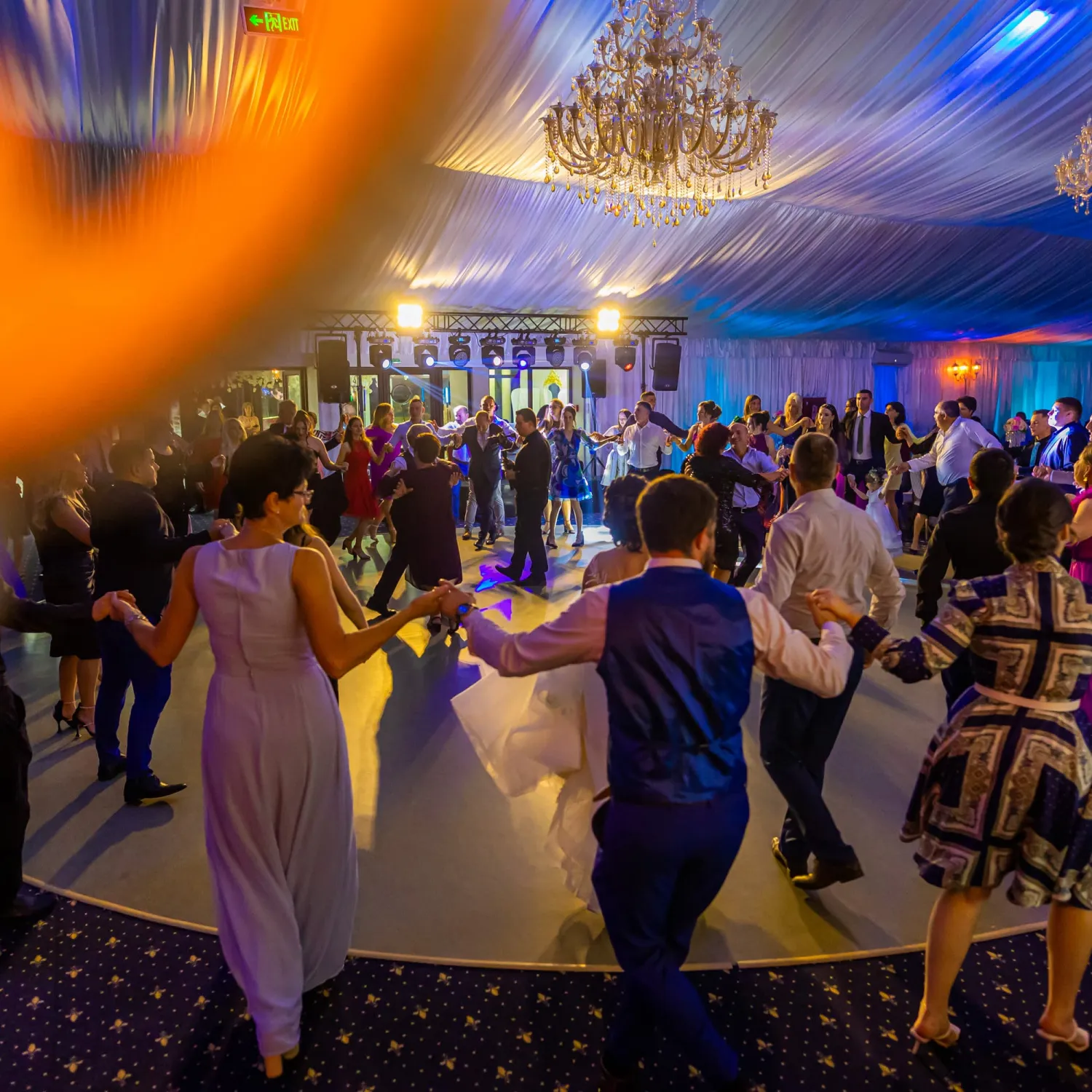 Petrecere de nuntă cu invitați dansând într-o sală de evenimente elegant decorată, sub luminile colorate ale ringului de dans. Fotografie de Flaviu Studio surprinde veselia și atmosfera vibrantă a serii.