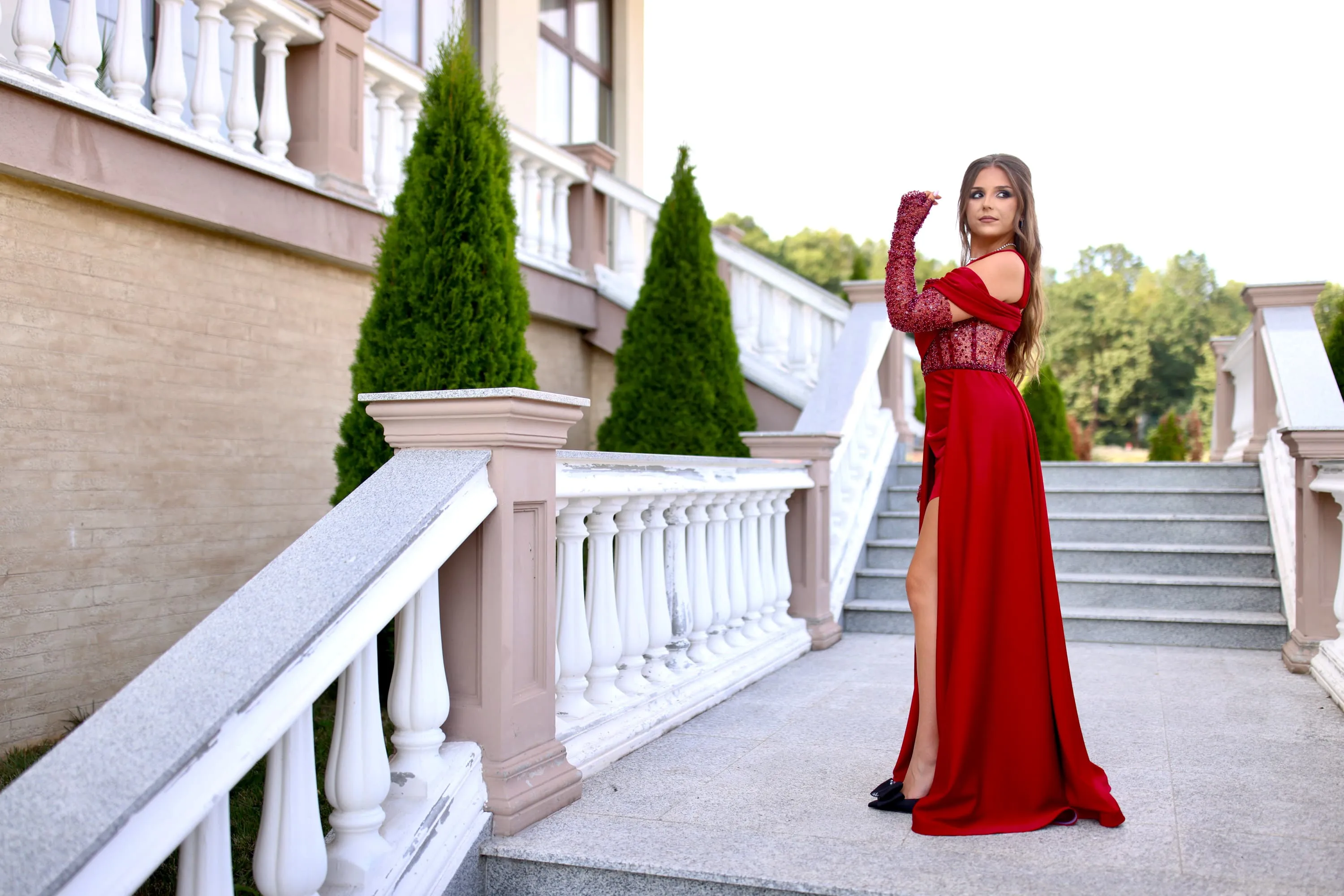 Fotografie de majorat cu Ariana purtând o rochie roșie, pozând elegant pe o scară exterioară decorată cu verdeață. Realizată de Flaviu Studio.