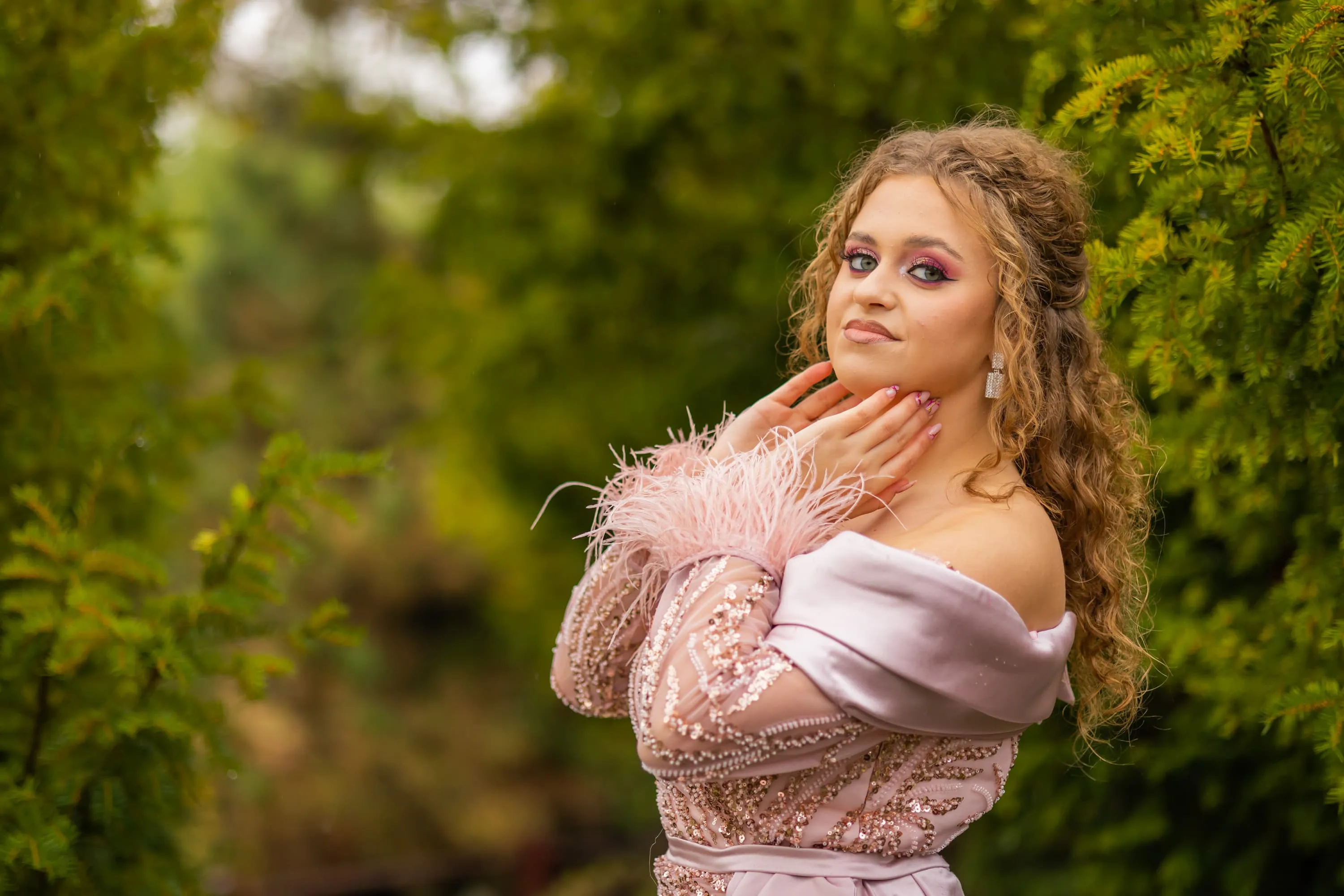 Fotografie de majorat cu Alexandra purtând o rochie roz pal cu pene, zâmbind și pozând în mijlocul unei grădini verzi. Realizată de Flaviu Studio.