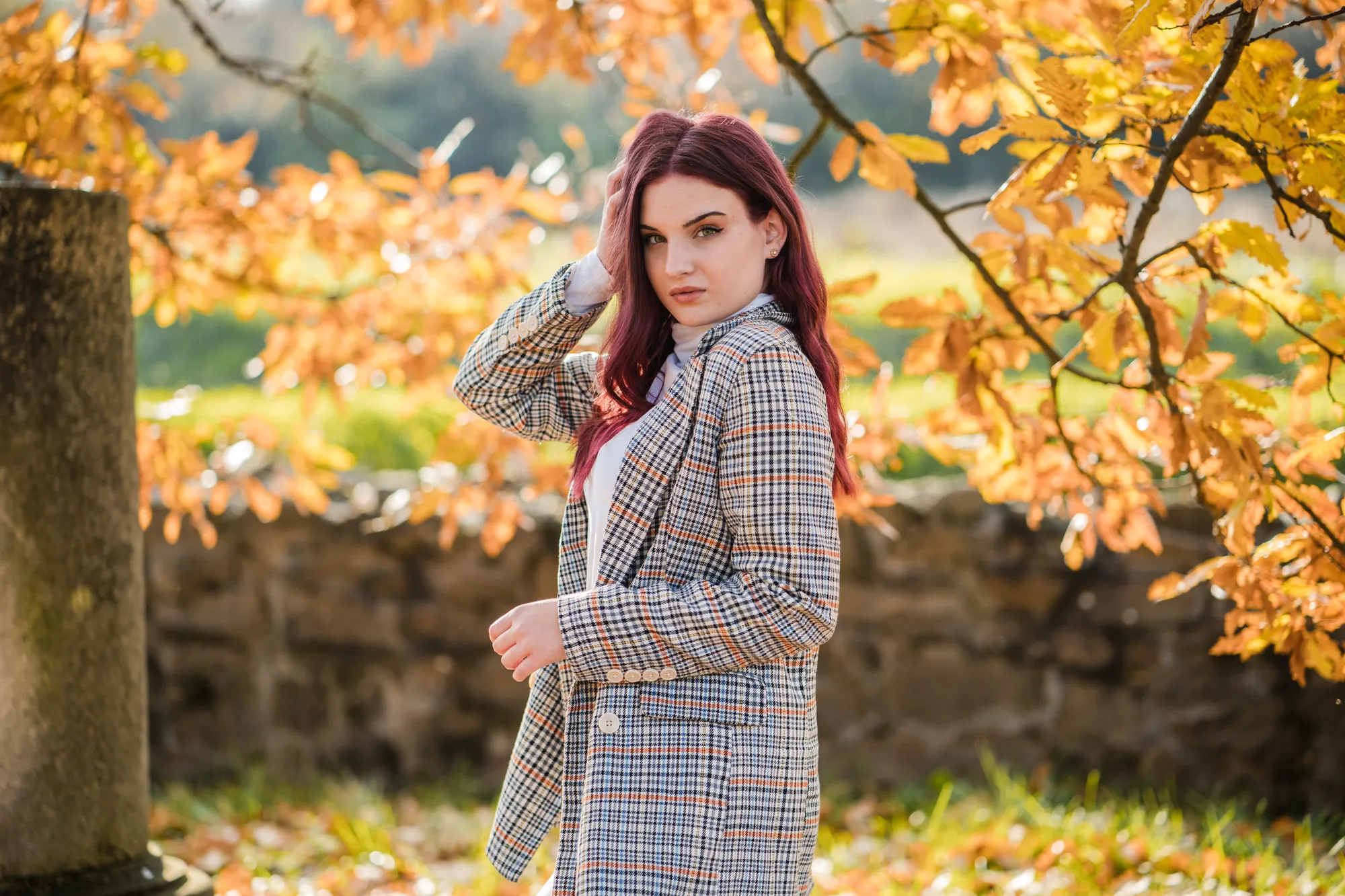 Fotografie de absolventă realizată de Flaviu Studio, capturând o tânără în mijlocul unui peisaj tomnatic. Cu părul roșcat și o ținută modernă, absolventa emană încredere și stil, completate de lumina blândă a toamnei și frunzele aurii care oferă o atmosferă caldă și vibrantă.
