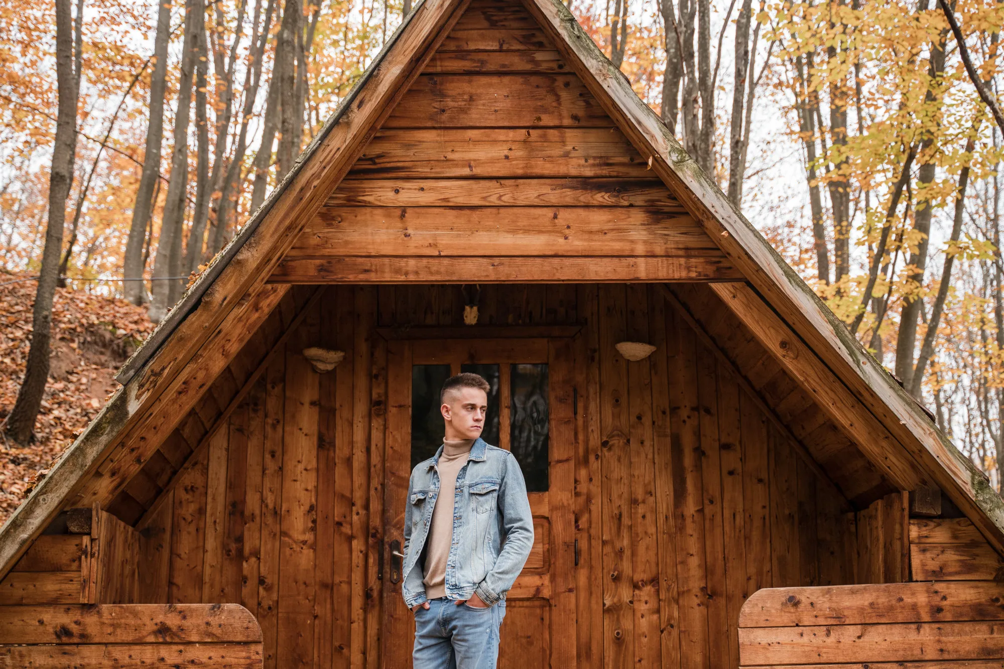 Portret de absolvent clasa a XII-a realizat de Flaviu Studio – tânăr pozând în fața unei cabane din lemn, într-un peisaj de toamnă ce simbolizează maturitatea și începutul unei noi etape.