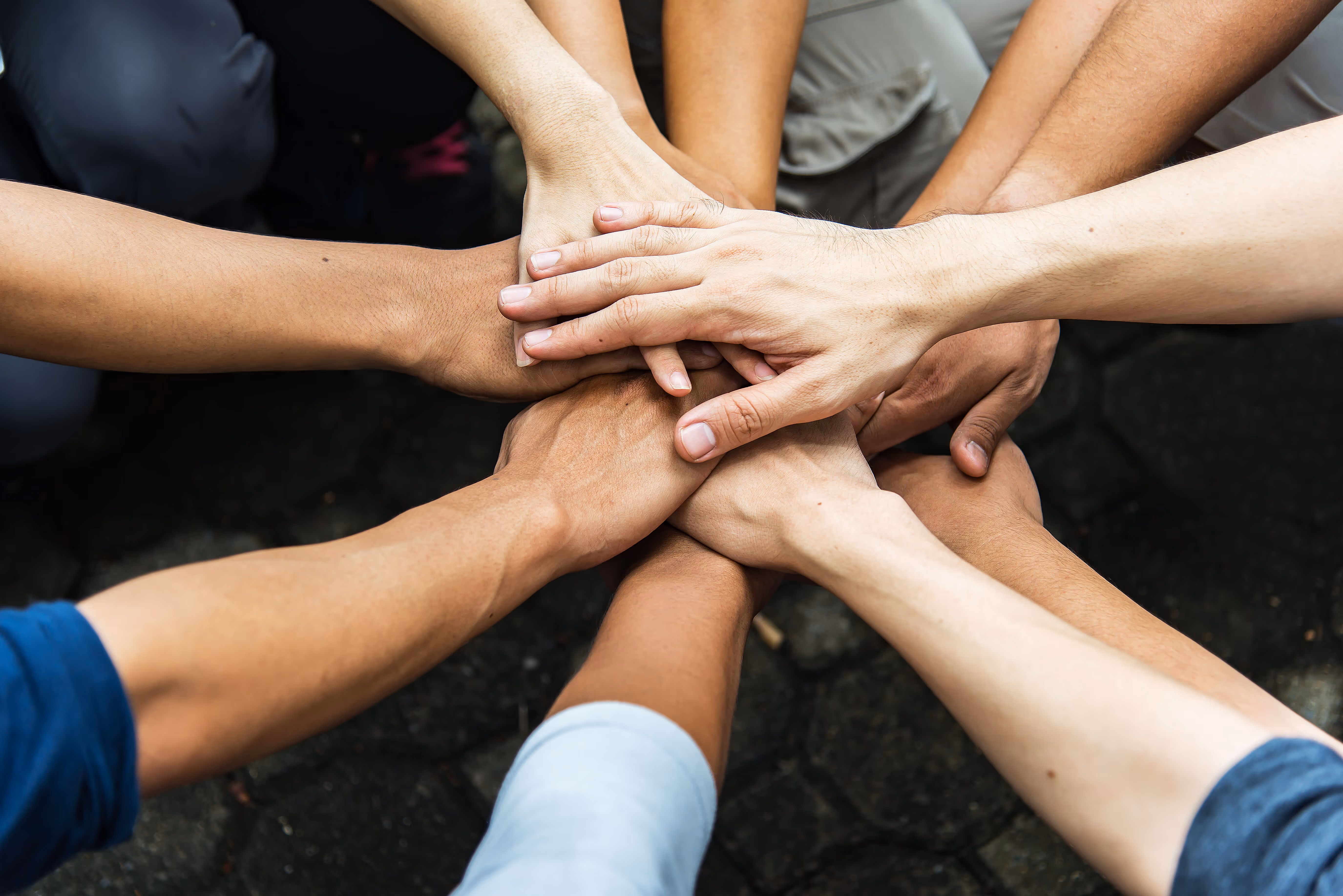 Mehrere Hände unterschiedlicher Hautfarben, die gestapelt für Teamwork zusammengelegt sind.