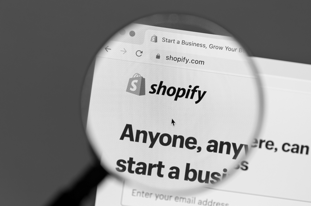 The Shopify logo and website is shown through a magnifying glass.