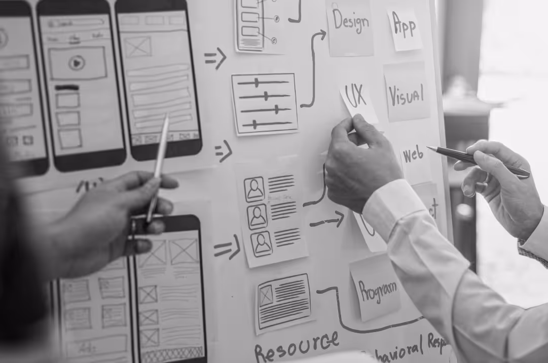 Two people stand in front of a whiteboard mapping out development stages for a mobile app.