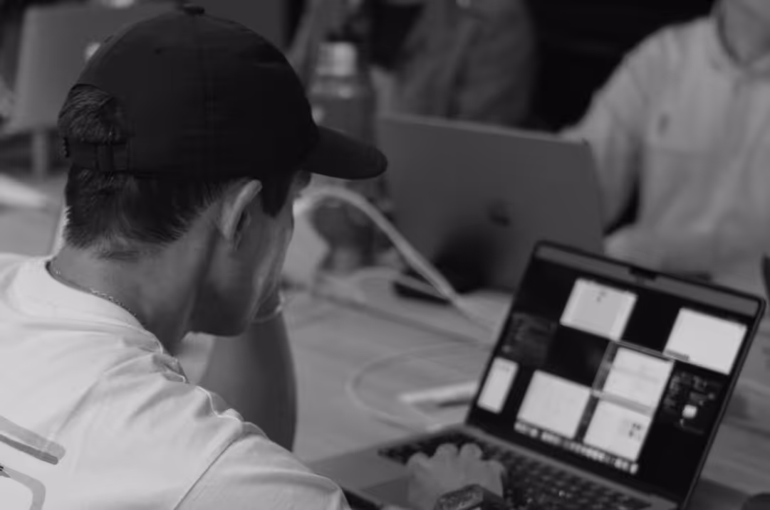 A man wearing a cap works at a laptop.