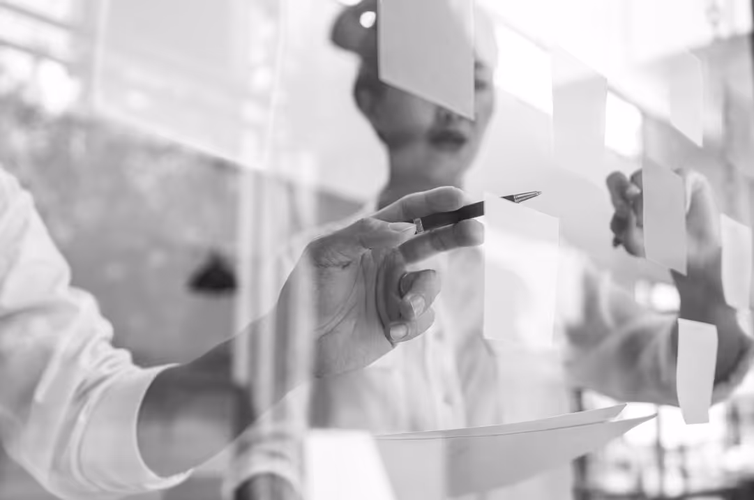 Two people stand in front of a glass surface, pointing at sticky notes.