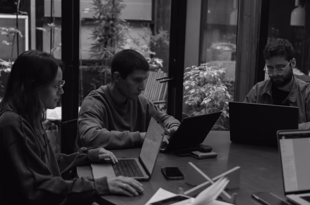 Three people sit around a table working on their laptops.