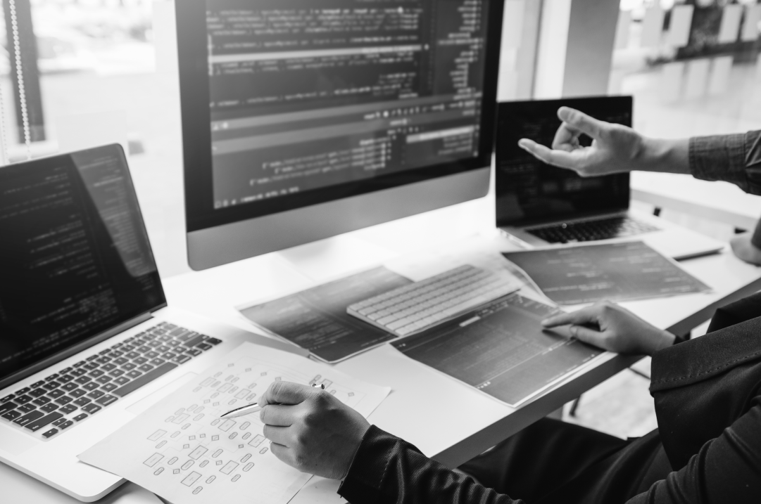 A hand points to a monitor in between two laptops.