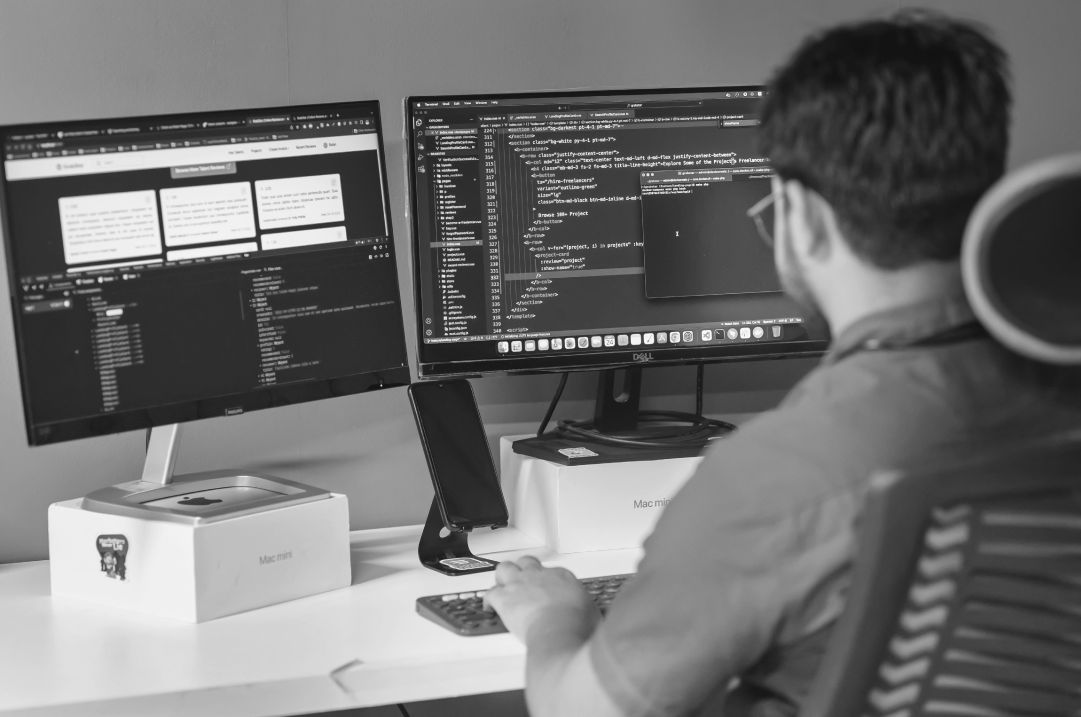 A man works in an office with two monitors that display code and documents.