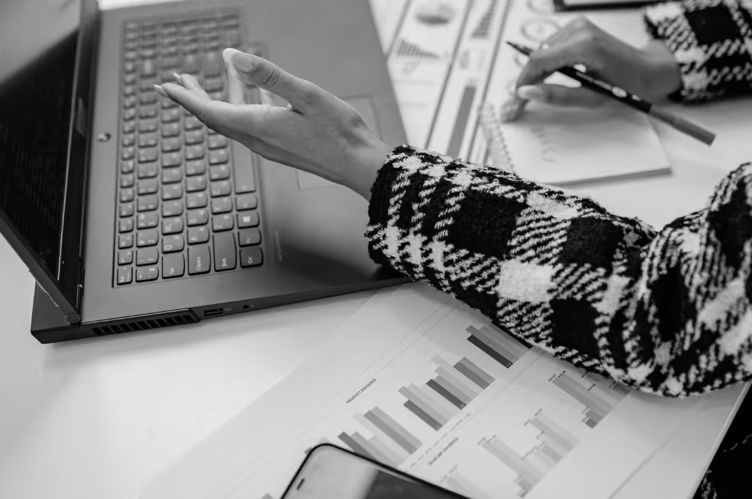 A manicured hand in a houndstooth jacket gestures above a laptop.