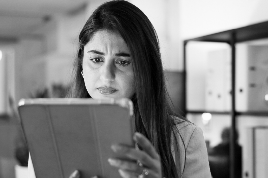 A woman holds a tablet in her hands, staring at it with a displeased expression.