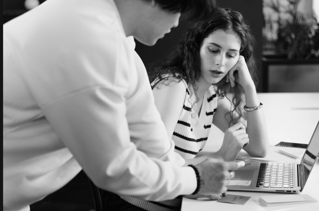 Two people lean over a laptop while conversing.