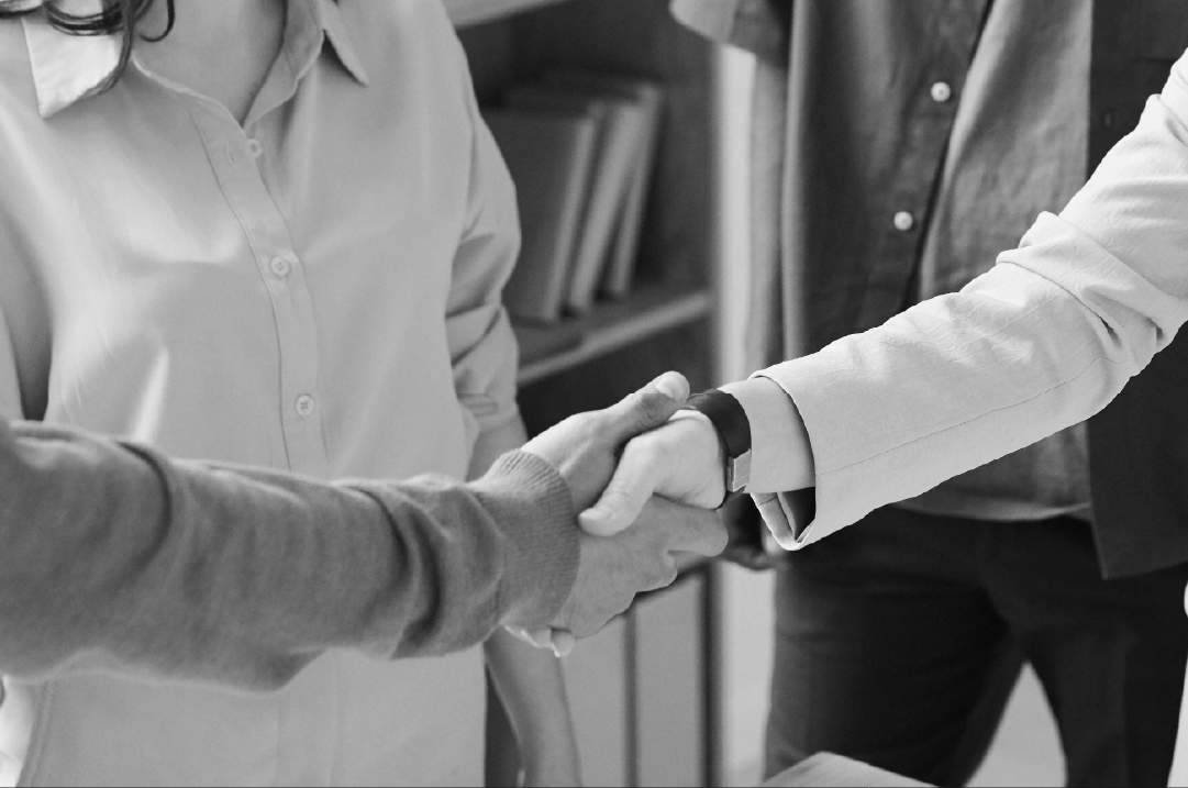 Two people shake hands while two other people stand off to the side.