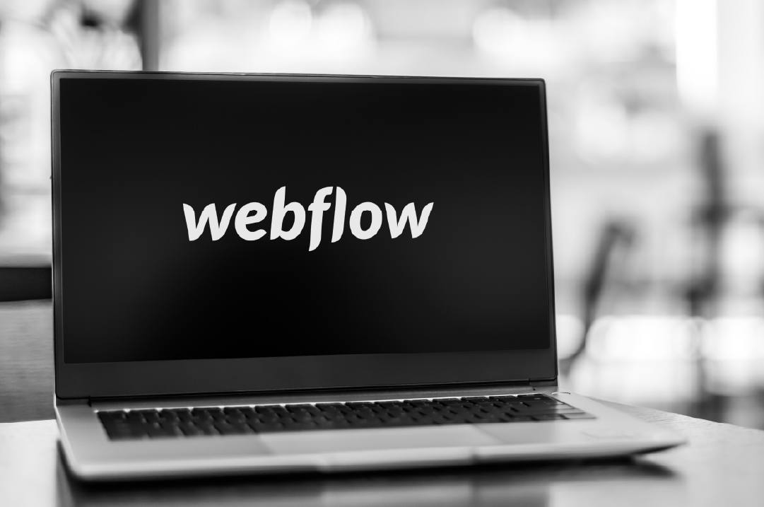 A laptop displays the Webflow wordmark on a black screen.