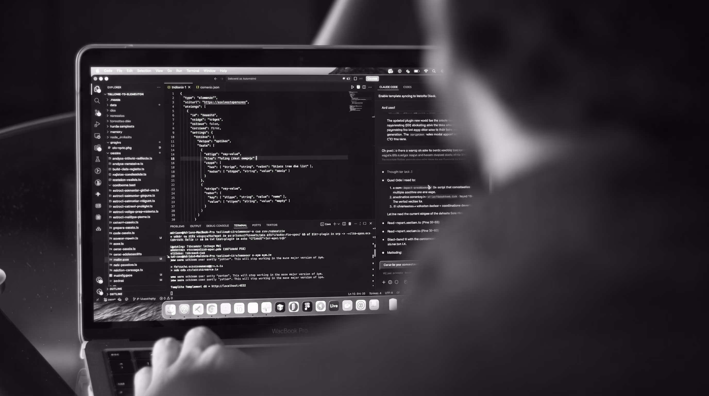 Black-and-white photo of a developer's hands typing on a laptop, with a code editor open showing project files and lines of code on screen.