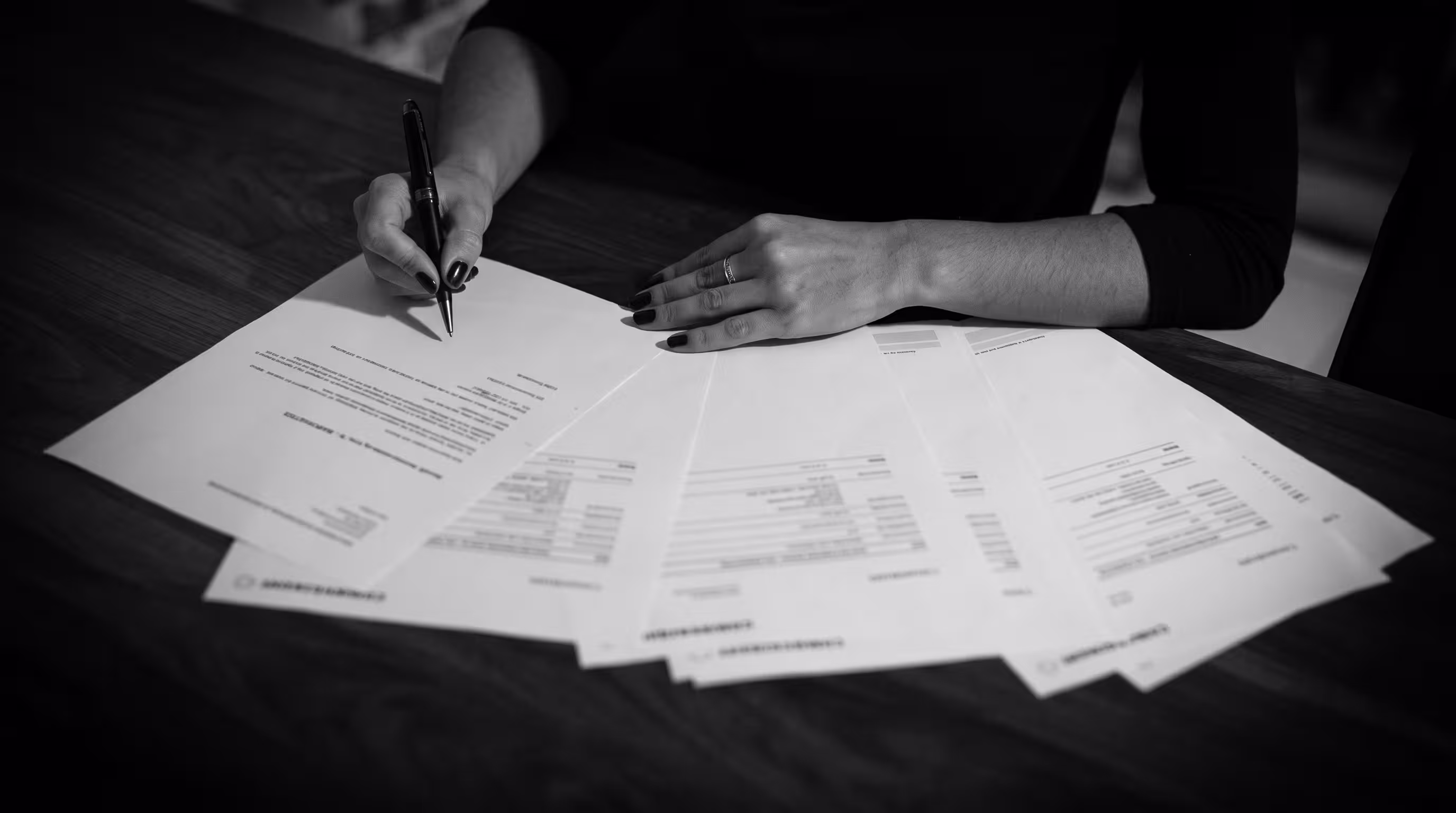 Close-up of hands signing paperwork with printed reports spread across a table"