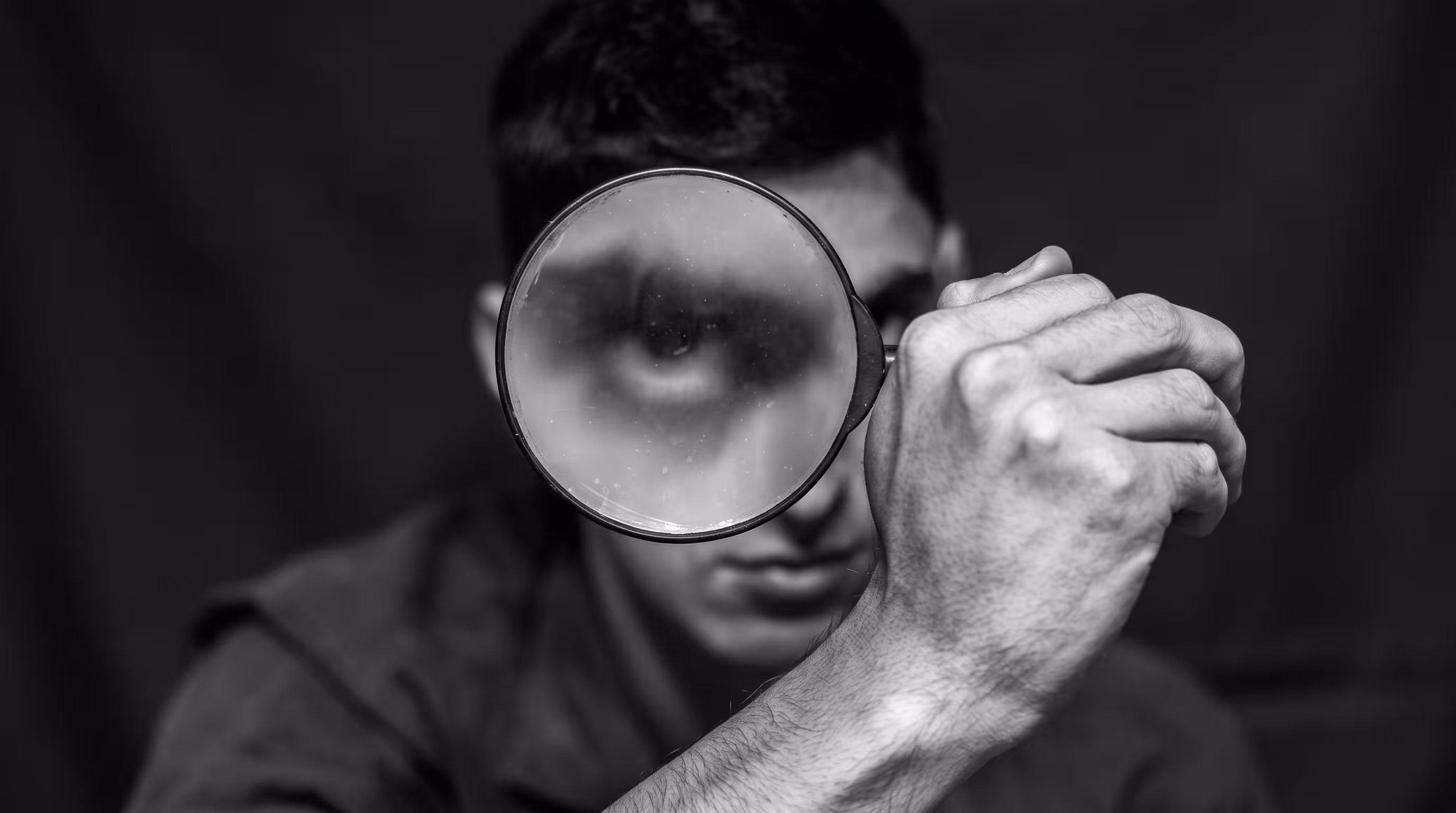 Person looking through a magnifying glass, face distorted, black and white
