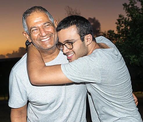 A happy older man and his son with Autism Spectrum Disorder hug in front of a sunset